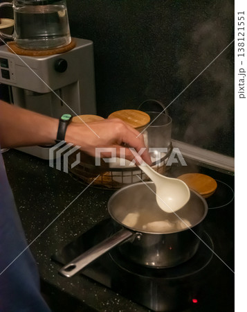 Man cooking soup in pot on induction stove in kitchen. Person using ladle to stir boiling liquid meal. Culinary process, homemade dinner preparation, domestic lifestyle concept. Man cooking soup in pot on induction stove in kitchen. Person using ladle to stir boiling liquid meal. Culinary process, homemade dinner preparation, domestic lifestyle concept. 138121551