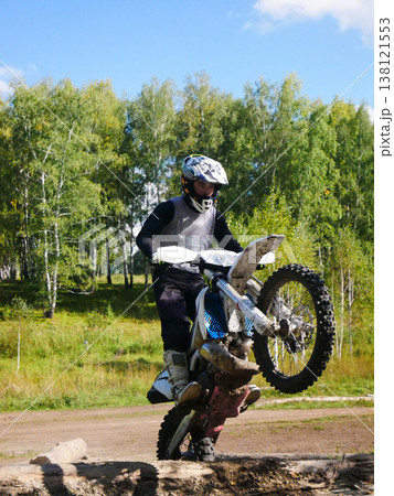 Man motorcyclist performing wheelie on dirt bike in forest. Professional enduro rider on motocross motorcycle during training outdoor. Extreme sport, speed, adrenaline and adventure concept. Man motorcyclist performing wheelie on dirt bike in forest. Professional enduro rider on motocross motorcycle during training outdoor. Extreme sport, speed, adrenaline and adventure concept. 138121553
