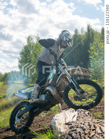 Motocross rider man overcoming obstacle on dirt bike in forest. Extreme athlete practicing enduro riding. Professional biker jumping over log on motorcycle. Action power sport concept. 138121560