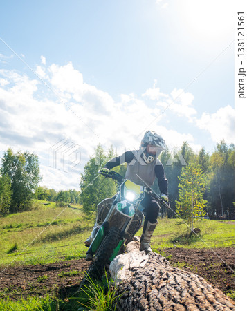 Man riding dirt bike over log on off-road trail. Motocross racer competing in enduro race on forest course. Extreme outdoor sport, adventure travel concept and professional athlete activity. Man riding dirt bike over log on off-road trail. Motocross racer competing in enduro race on forest course. Extreme outdoor sport, adventure travel concept and professional athlete activity. 138121561