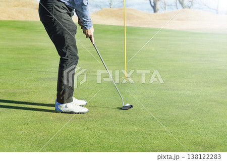 グリーンのカップへ向かうゴルフボールとパターの足元カット 138122283