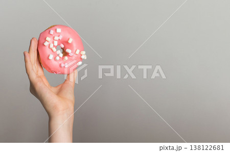 Pink Donut with white marshmallows in human hand, sweet dessert Pink Donut with white marshmallows in human hand, sweet dessert 138122681