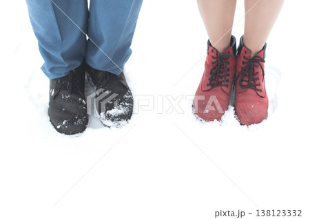 Two people stand together in snow with one wearing black shoes and the other in red boots. 138123332