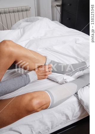 a man smooths a compression sock on his leg 138125348