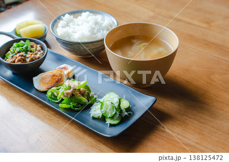 木のテーブルの和朝食定食 ご飯と味噌汁と納豆と漬物と長皿のおかず 138125472