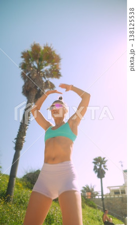Relaxed woman posing beneath palm tree with vintage visor in coastal area Relaxed woman posing beneath palm tree with vintage visor in coastal area 138125538