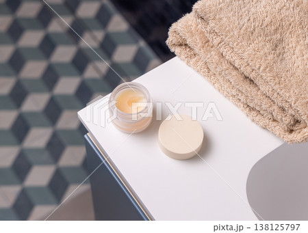 Opened handmade lip balm jar in blue bathroom with towel. Blank lid cosmetic mockup 138125797