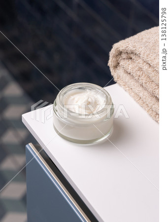 Opened cosmetic cream glass jar near beige bath towel against blue tiled floor top view 138125798