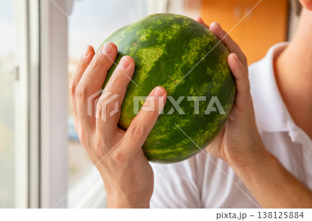 A small, round, ripe watermelon in a man's hands. Green striped watermelon, organic farming. A small, round, ripe watermelon in a man's hands. Green striped watermelon, organic farming. 138125884