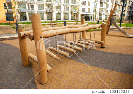 Modern wooden rope bridge on a children's playground. Outdoor entertainment and childhood adventure concept. Safe play equipment for kids. Modern wooden rope bridge on a children's playground. Outdoor entertainment and childhood adventure concept. Safe play equipment for kids. 138125888