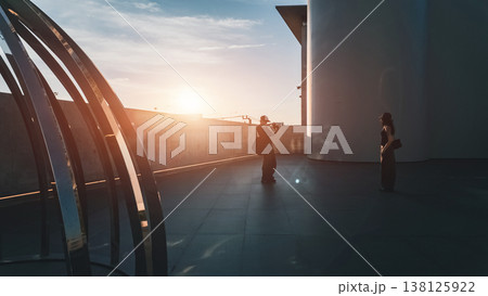 Man photographing woman at sunset in modern urban space with warm light, Couple creating memories during golden hour with silhouette and cinematic atmosphere Man photographing woman at sunset in modern urban space with warm light, Couple creating memories during golden hour with silhouette and cinematic atmosphere 138125922