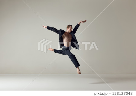 Male dancer captured in sideways jump with extended arms in minimal studio setting 138127048