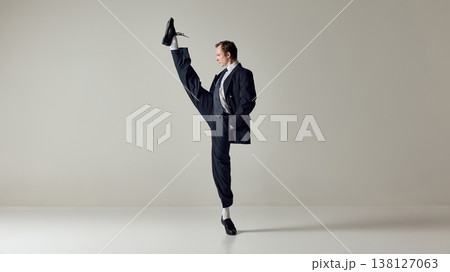 Businessman performing high kick while balancing in formal suit on neutral background. Businessman performing high kick while balancing in formal suit on neutral background. 138127063