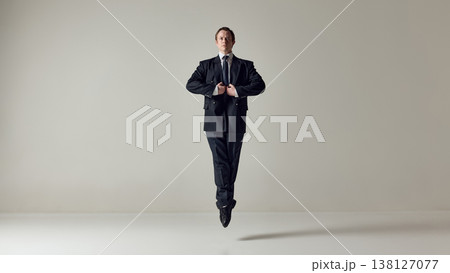 Businessman floating upright while fixing jacket on neutral background. Businessman floating upright while fixing jacket on neutral background. 138127077