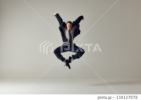 Businessman jumping with arms raised in expressive motion on neutral background. 138127078