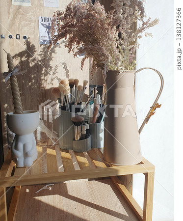 Organizer with makeup brushes and decorative vase with dried flowers on a wooden shelf 138127366