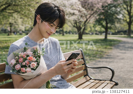 花束を持ってスマートフォンを確認する男性（待ち合わせ・連絡待ち・恋愛シーン） 138127411