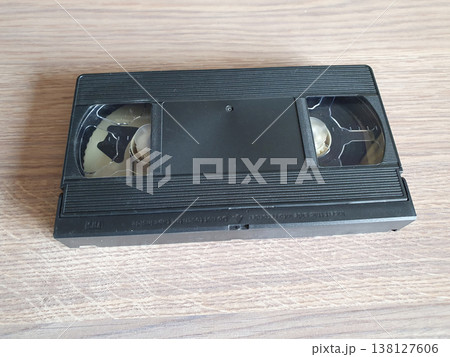 Black retro VHS video cassette lying on a wooden surface. Close-up of the back side of the analog video information carrier. Black retro VHS video cassette lying on a wooden surface. Close-up of the back side of the analog video information carrier. 138127606
