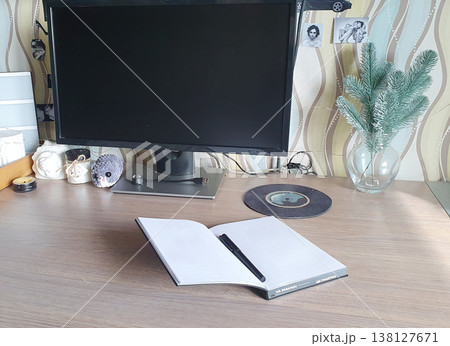 Cozy workplace at home: open notebook with pen on wooden table in front of computer monitor. Atmosphere of productivity, study and hobby. Cozy workplace at home: open notebook with pen on wooden table in front of computer monitor. Atmosphere of productivity, study and hobby. 138127671