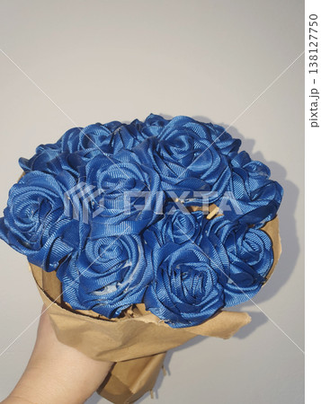 Hand holding a bouquet of blue roses made from satin ribbons wrapped in craft paper 138127750