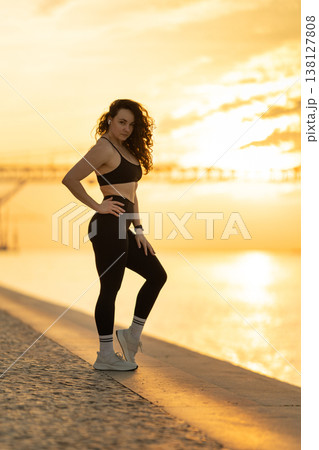 Confident woman standing riverside at golden hour sunrise 138127808