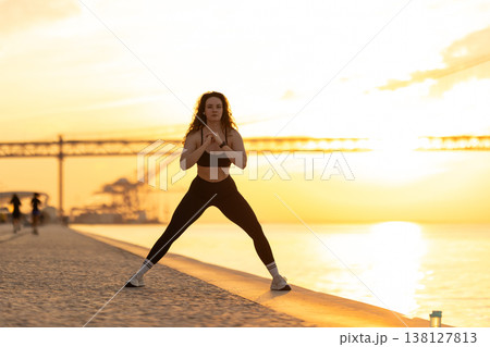 Woman exercising outdoors doing squats at sunset Woman exercising outdoors doing squats at sunset 138127813