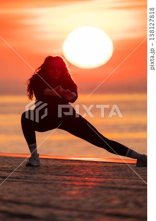 Woman doing stretching exercise at vibrant sunset sea Woman doing stretching exercise at vibrant sunset sea 138127818