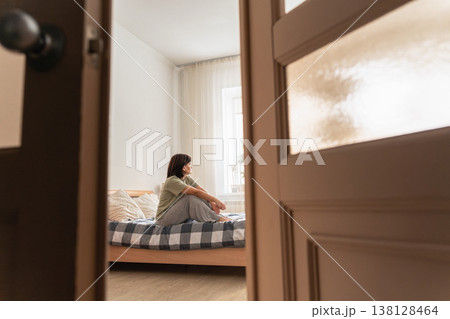An adult woman sitting on bed, struggling with sadness, grief, and mental health issues. Feeling lonely and isolated 138128464