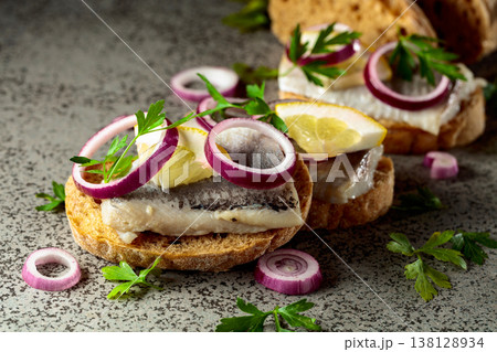 Open sandwiches with herring filet, red onion, lemon, and parsley. 138128934