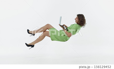 Woman floating while using laptop isolated on white background lifestyle studio shot. Woman floating while using laptop isolated on white background lifestyle studio shot. 138129452