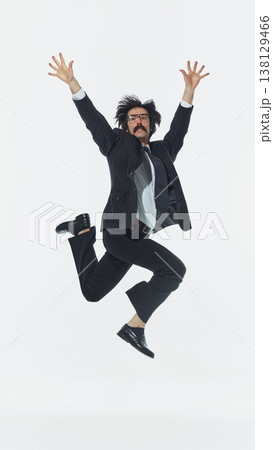 Man in formal outfit jumping with arms raised in energetic motion in studio. Man in formal outfit jumping with arms raised in energetic motion in studio. 138129466