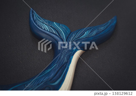 Close-up of a carved wooden whale tail featuring intricate blue carved patterns and textures on a dark background. Close-up of a carved wooden whale tail featuring intricate blue carved patterns and textures on a dark background. 138129612