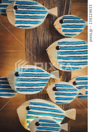 Close-up of a group of hand-painted blue and white striped wooden fish attached to a rustic timber base. Close-up of a group of hand-painted blue and white striped wooden fish attached to a rustic timber base. 138129633