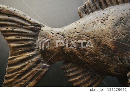 Macro shot of a hand-carved wooden fish sculpture's tail section, highlighting deep weathered textures and natural timber grain. Macro shot of a hand-carved wooden fish sculpture's tail section, highlighting deep weathered textures and natural timber grain. 138129651