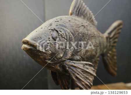 Close-up perspective view of a hand-carved wooden fish sculpture, highlighting the detailed weathered head and textured fins on a dark background. Close-up perspective view of a hand-carved wooden fish sculpture, highlighting the detailed weathered head and textured fins on a dark background. 138129653