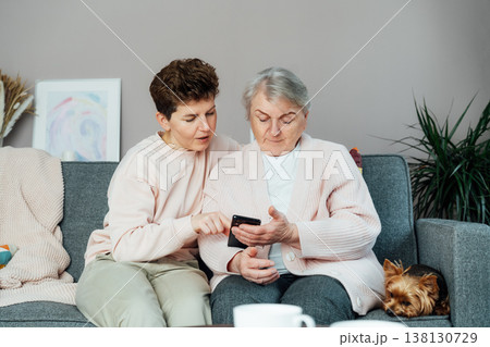 Adult woman explaining her senior mother how to use smartphone. Education for aged. Retired lady discovering mobile technology for calling, texting, buying online, playing games, using medical apps Adult woman explaining her senior mother how to use smartphone. Education for aged. Retired lady discovering mobile technology for calling, texting, buying online, playing games, using medical apps 138130729