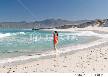 Woman in red swimsuit walking on beach 138130949