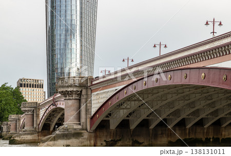 The ornate, scarlet-hued arches of Blackfriars Bridge sweep gracefully across the frame, their Victorian grandeur punctuated by golden medallions and classical stone piers. The ornate, scarlet-hued arches of Blackfriars Bridge sweep gracefully across the frame, their Victorian grandeur punctuated by golden medallions and classical stone piers. 138131011