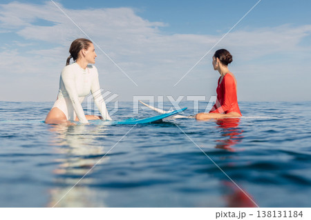 Two women surfers on surfboards in calm ocean waiting for surfing waves Two women surfers on surfboards in calm ocean waiting for surfing waves 138131184