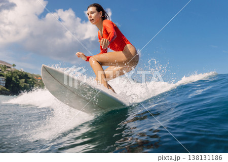 Surfer woman in swimsuit riding wave with splashes in tropical ocean Surfer woman in swimsuit riding wave with splashes in tropical ocean 138131186