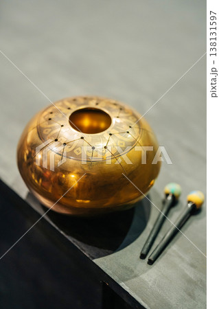 Golden Singing Bowl On Wooden Table, Engraved Mandala Pattern, Three Felt Mallets Beside Bowl, Warm Golden Singing Bowl On Wooden Table, Engraved Mandala Pattern, Three Felt Mallets Beside Bowl, Warm 138131597