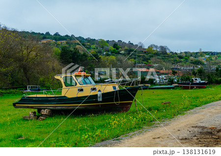 Derelict Cruiser On Grassy Riverbank, Weathered Hull With Peeling Paint And Rust, Moored Dinghies . Derelict Cruiser On Grassy Riverbank, Weathered Hull With Peeling Paint And Rust, Moored Dinghies . 138131619