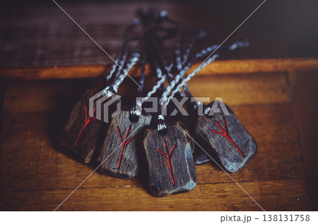 A horizontal pile of handcrafted wooden Algiz rune pendants with red carved symbols and dark cords on a wooden surface. A horizontal pile of handcrafted wooden Algiz rune pendants with red carved symbols and dark cords on a wooden surface. 138131758