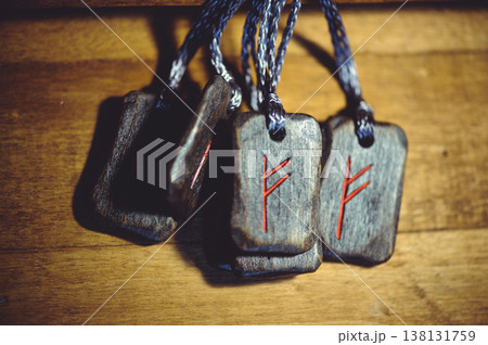 Horizontal group of handcrafted wooden Fehu rune pendants with red carved symbols and dark cords on a rustic wooden surface. 138131759
