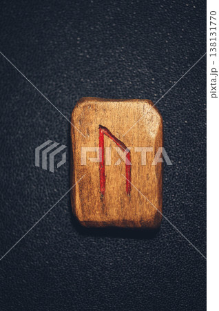 A vertical close-up of a handcrafted wooden Uruz rune stone, featuring the ancient symbol carved and filled with red pigment on a weathered grain. 138131770
