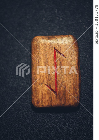 A vertical close-up of a handcrafted wooden Eihwaz rune stone, featuring the carved symbol filled with red pigment on a rustic grain. 138131778