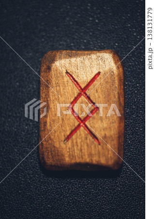 A vertical close-up of a handcrafted wooden Inguz rune stone, featuring the carved diamond-shaped symbol filled with red pigment on a rustic grain. A vertical close-up of a handcrafted wooden Inguz rune stone, featuring the carved diamond-shaped symbol filled with red pigment on a rustic grain. 138131779