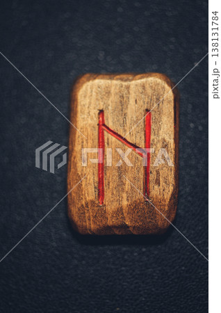 A vertical close-up of a handcrafted wooden Hagalaz rune stone, with the N-shaped symbol carved and filled with red pigment on a rustic grain. A vertical close-up of a handcrafted wooden Hagalaz rune stone, with the N-shaped symbol carved and filled with red pigment on a rustic grain. 138131784