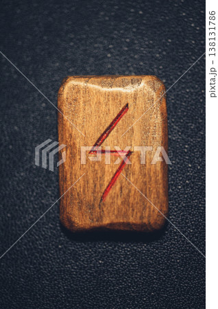 Vertical close-up of a handcrafted wooden Sowilo rune stone, featuring the carved sun symbol filled with red pigment on a rustic grain. 138131786