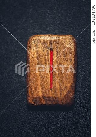 Vertical close-up of a handcrafted wooden Isa rune stone, with the single vertical ice symbol carved and filled with red pigment on a rustic grain. Vertical close-up of a handcrafted wooden Isa rune stone, with the single vertical ice symbol carved and filled with red pigment on a rustic grain. 138131790